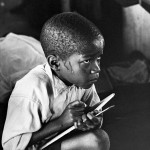 Earnest boy squats on haunches and strains to follow lesson in heat of packed classroom, 1960-1966 © The Ernest Cole Family Trust Courtesy of the Hasselblad Foundation, Gothenburg, Sweden